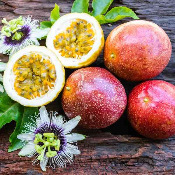 three panama red passionfruit and one halved panama red passionfruit and its flowers sitting on a wooden board